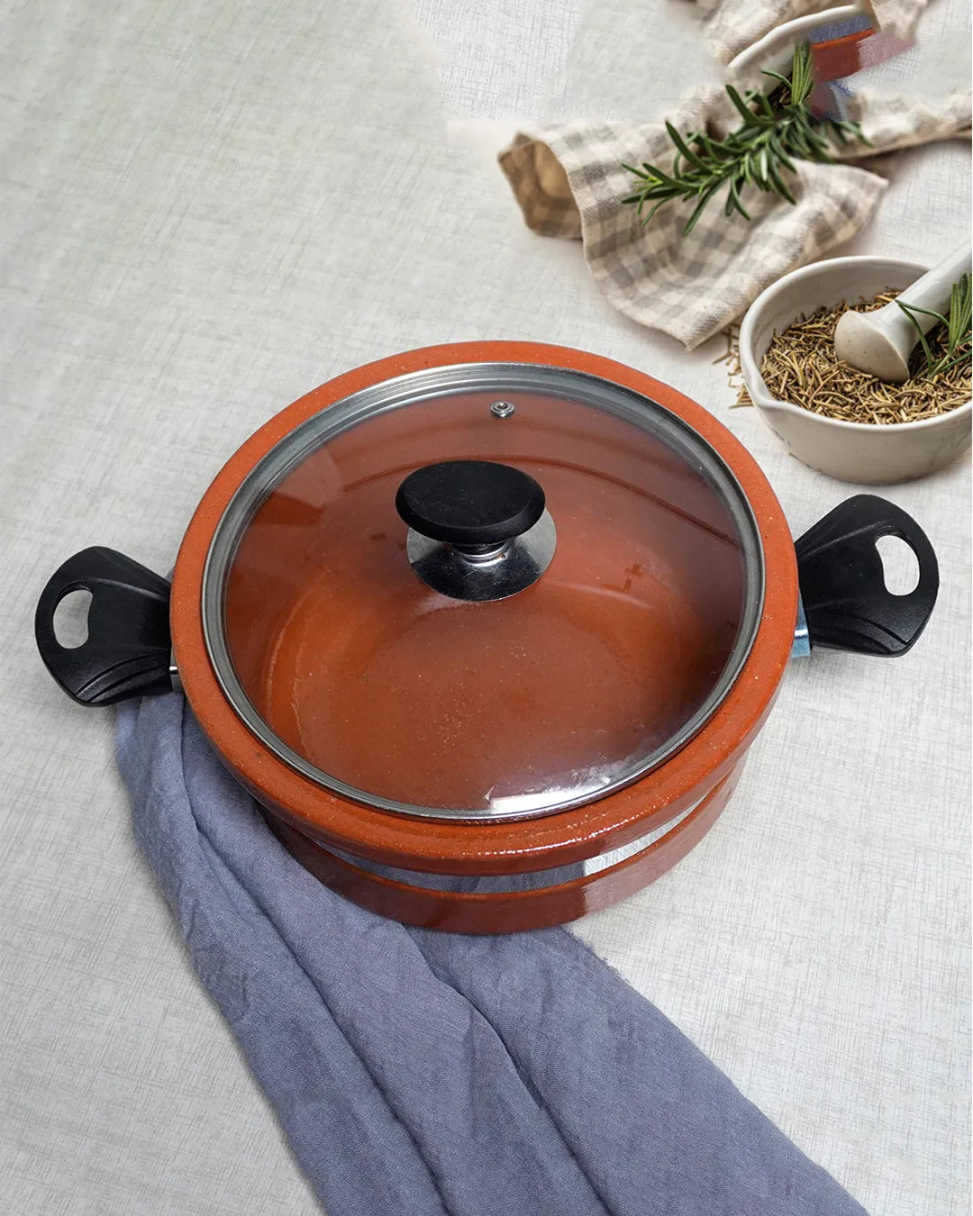 Ceramic pot with lid on a light gray surface with kitchen items in the background