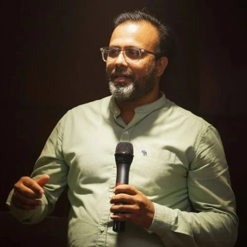 Man holding a microphone while speaking in a dark room.